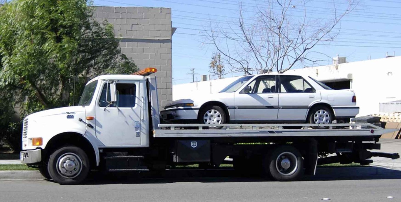 White sedan being towed on professional flatbed truck